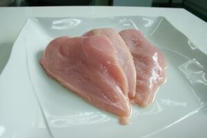 Immagine di pollo crudo su un tagliere, evidenziando il rischio di contaminazione batterica.